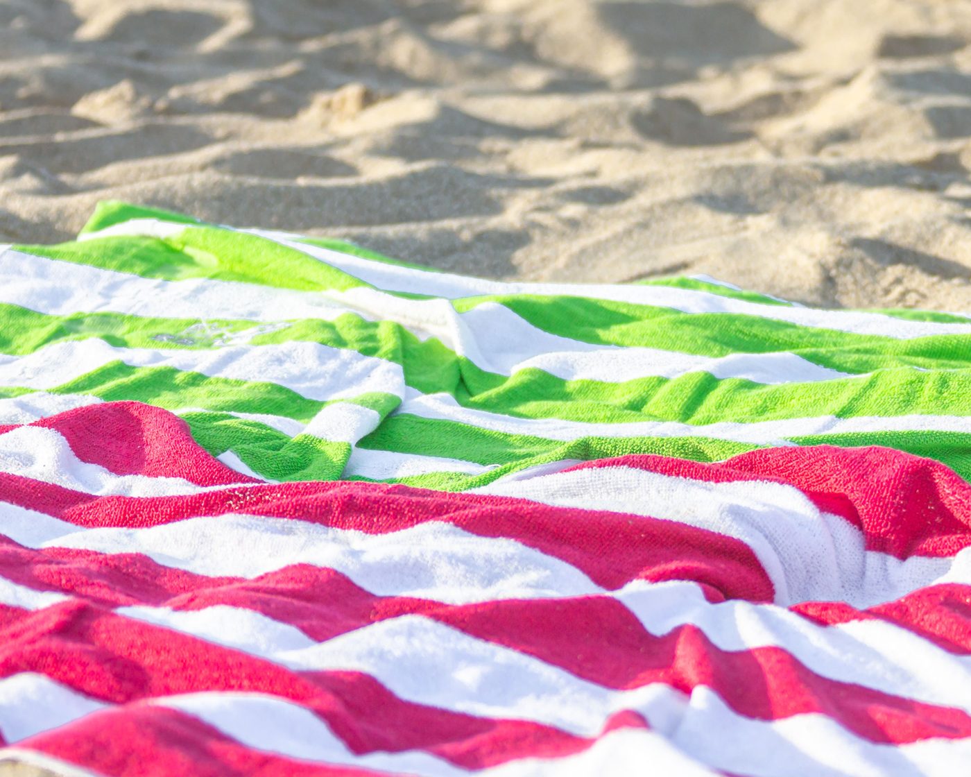 Bright pink, green, and white striped beach towels spread out on the sand