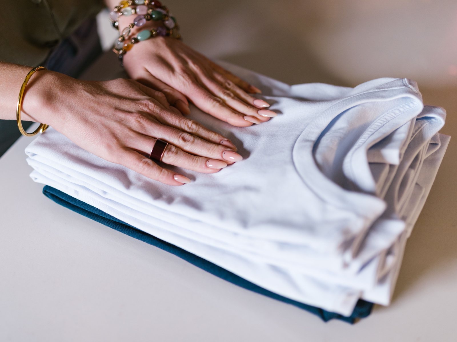 Hands smoothing a neat stack of freshly folded white T-shirts